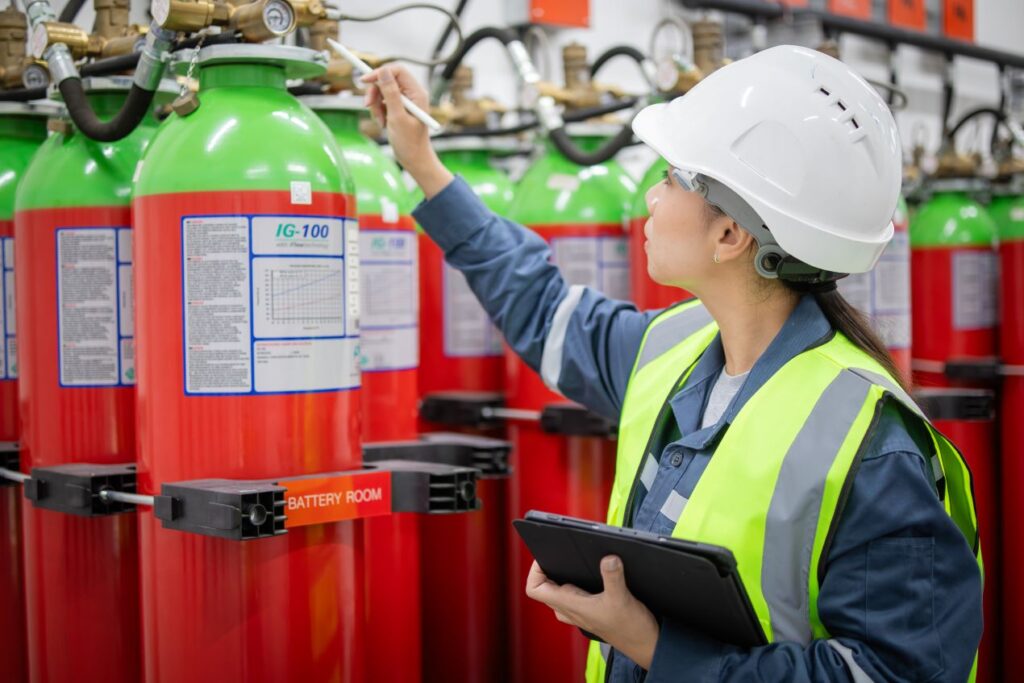 Ingenieurin mit Schutzhelm und Tablet prueft Gasloeschanlage im Technikraum, Arbeit eines Sachverstaendiger Loeschanlagen